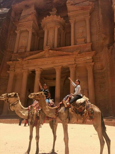 Two students riding camels with fist raised and smiling